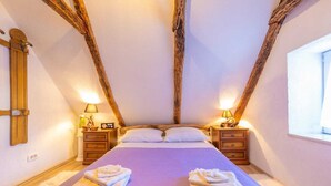 Una camera da letto con un letto grande, due comodini con lampade, un soffitto con travi in legno e una finestra a destra.