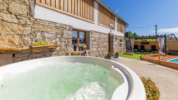 Un edificio in pietra con un balcone in legno, una vasca idromassaggio e un solarium con piscina.