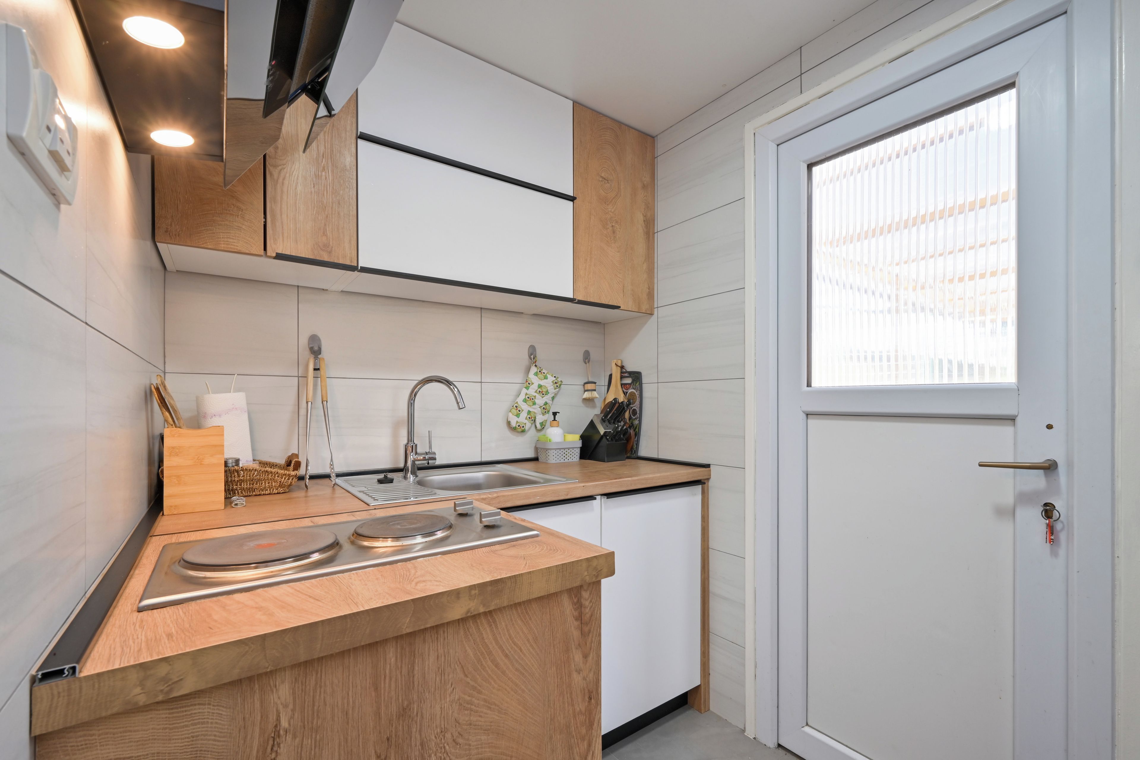 Une cuisine moderne dotée d’un plan de travail en bois, d’un évier en acier inoxydable et d’une fenêtre avec des stores.