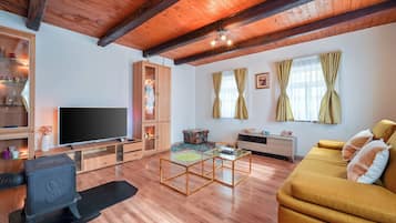 A modern living room with a wooden ceiling, a flat-screen TV, a sofa, a coffee table, and a cabinet.