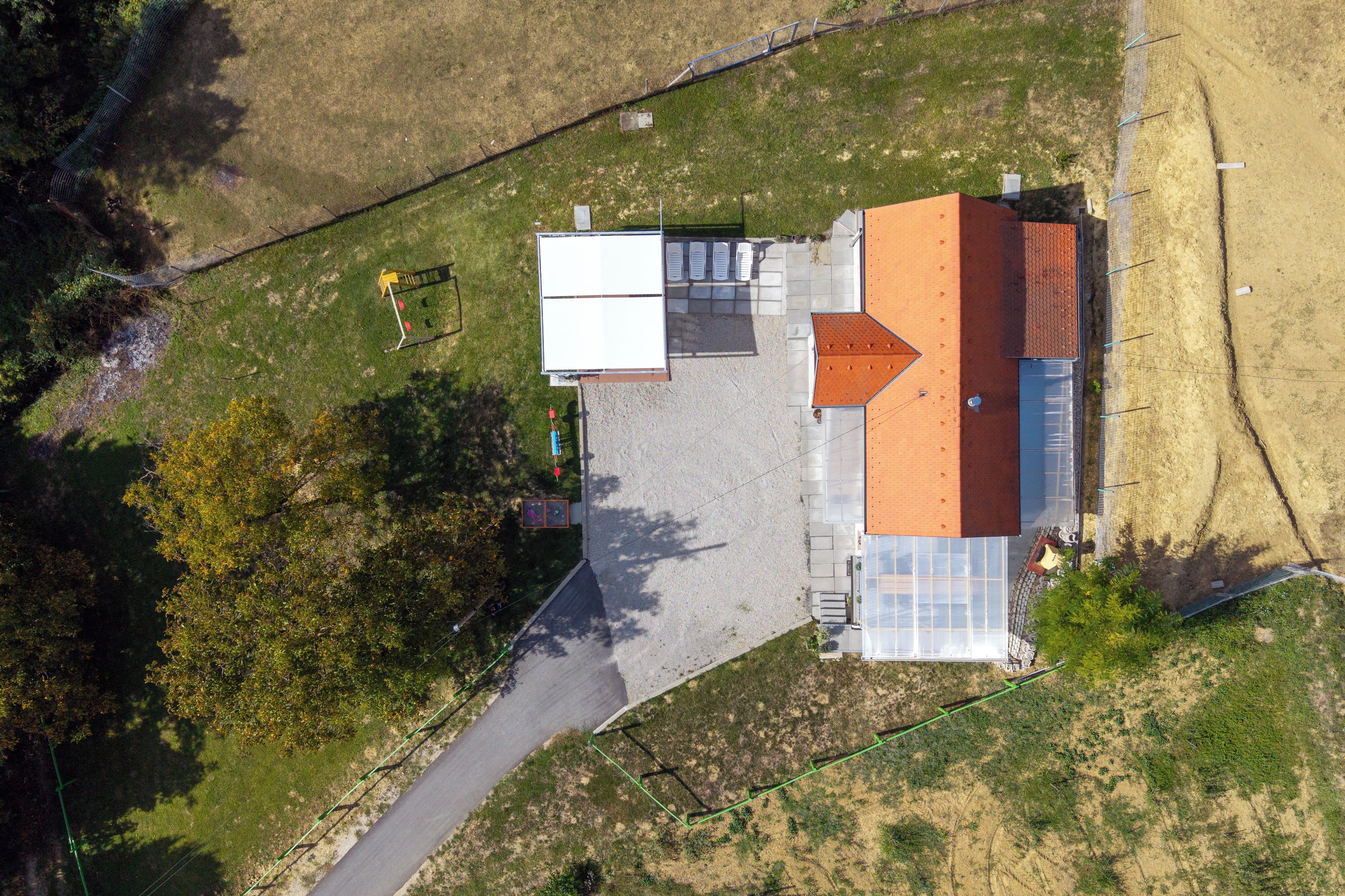 An aerial view of a building with a red roof, a paved driveway, and a fenced area with a yellow structure.