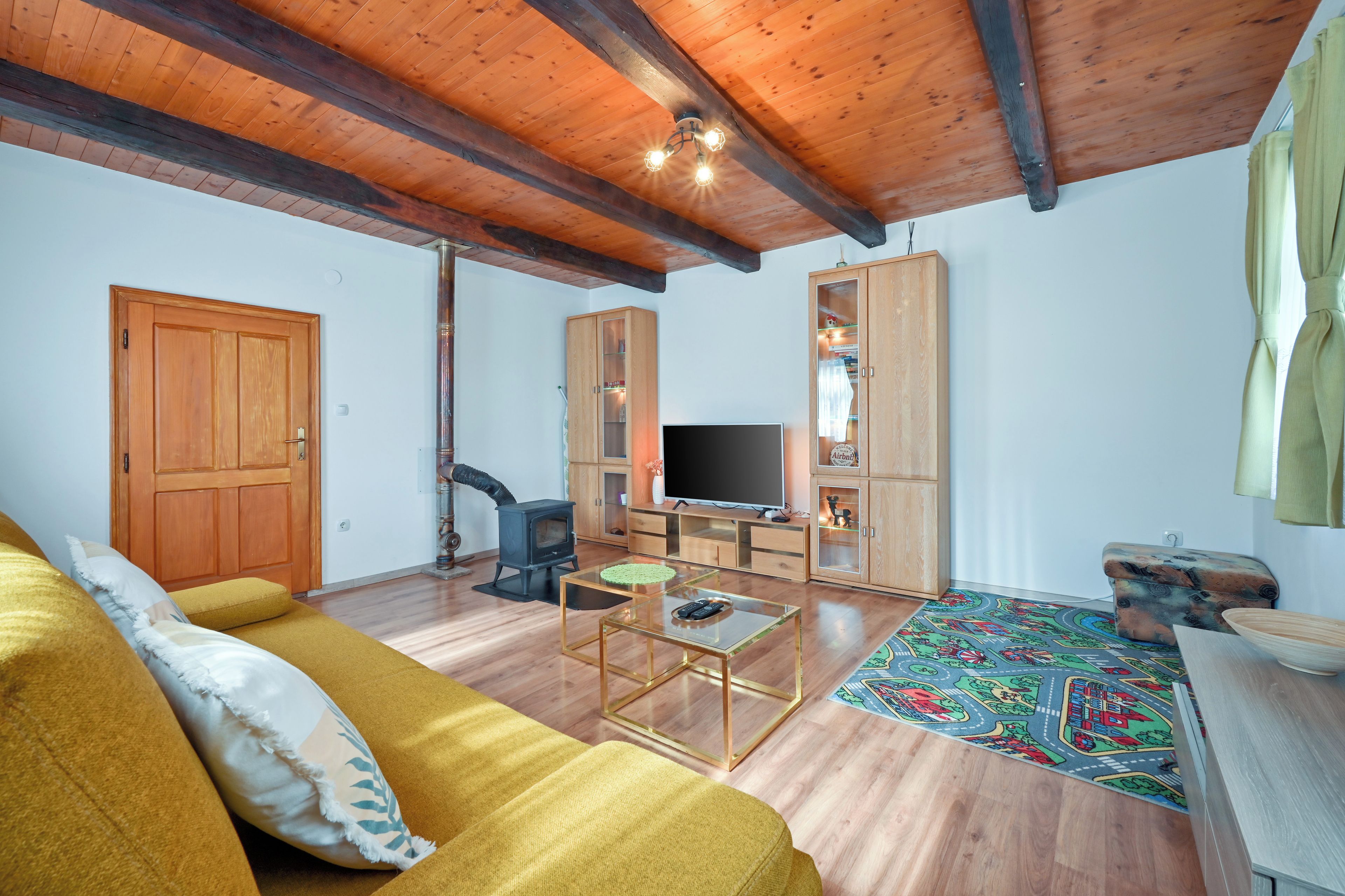 Un salon avec un canapé, un téléviseur, un plafond en bois et un tapis à motifs.