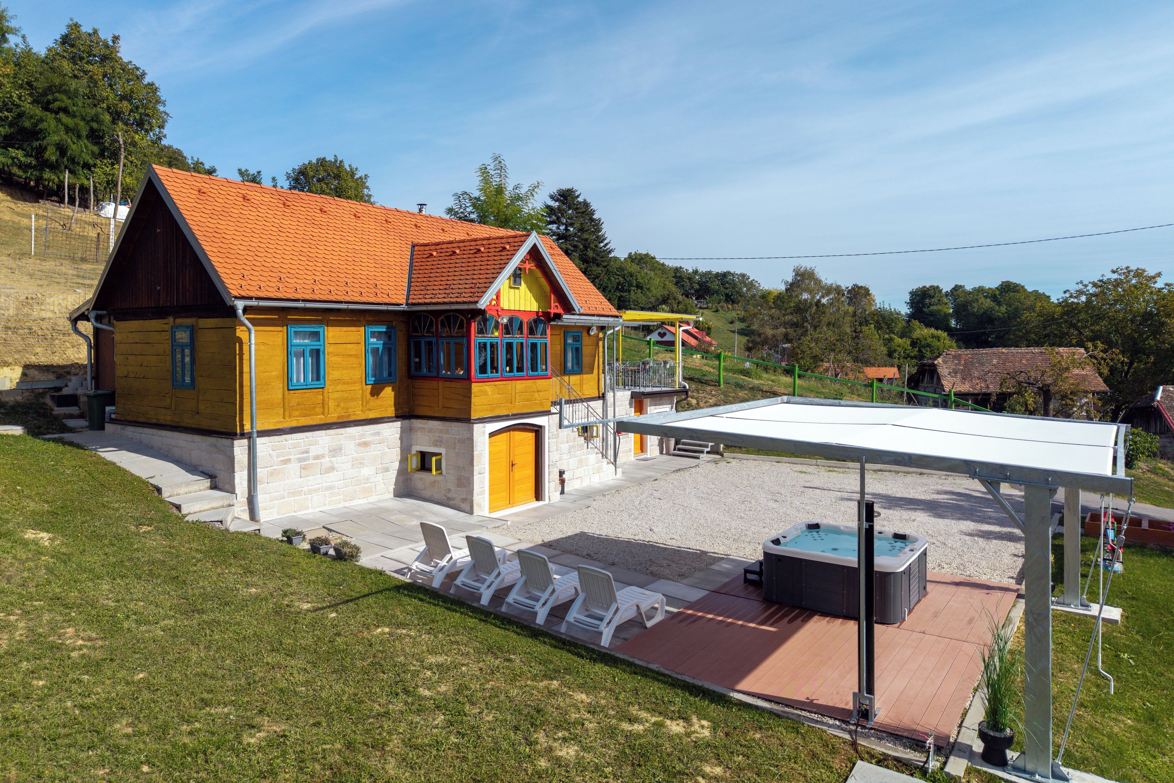 Une maison à deux étages avec un toit recouvert de tuiles rouges, un balcon et un espace extérieur aménagé avec des chaises blanches.