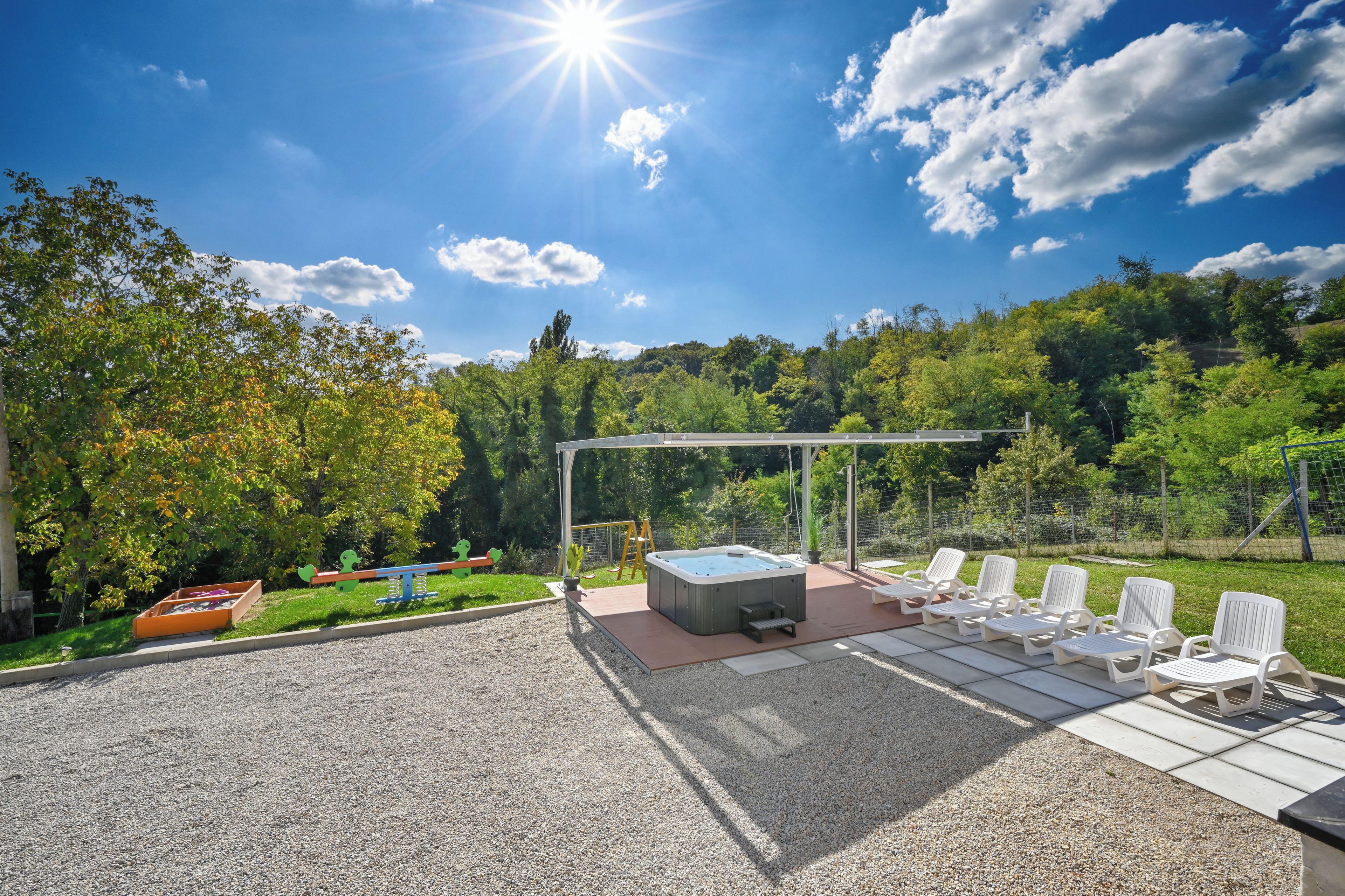 Un patio con un jacuzzi, sillas de descanso y un columpio.