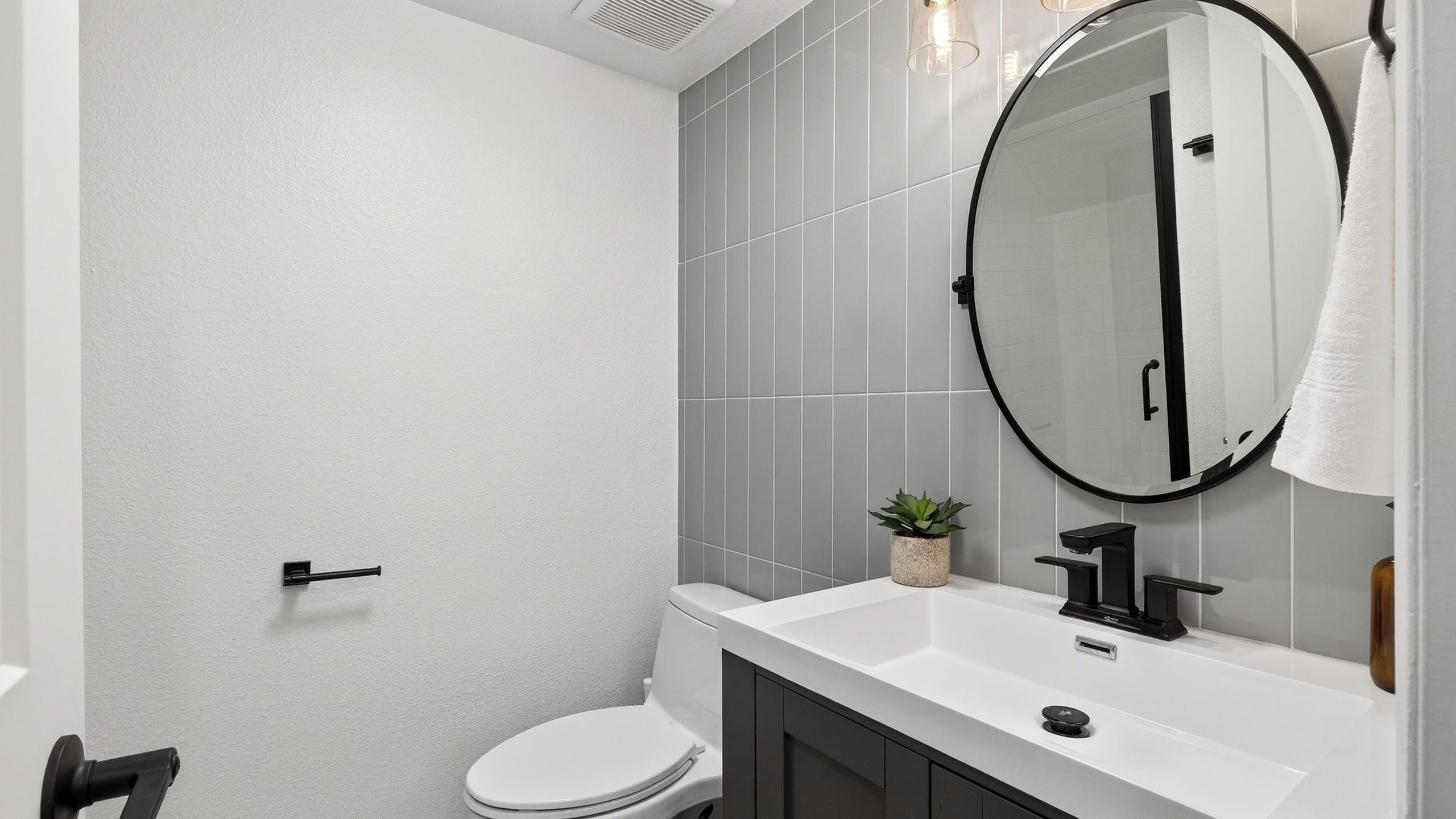 Un baño moderno con inodoro, lavabo, espejo y una pequeña planta en maceta.