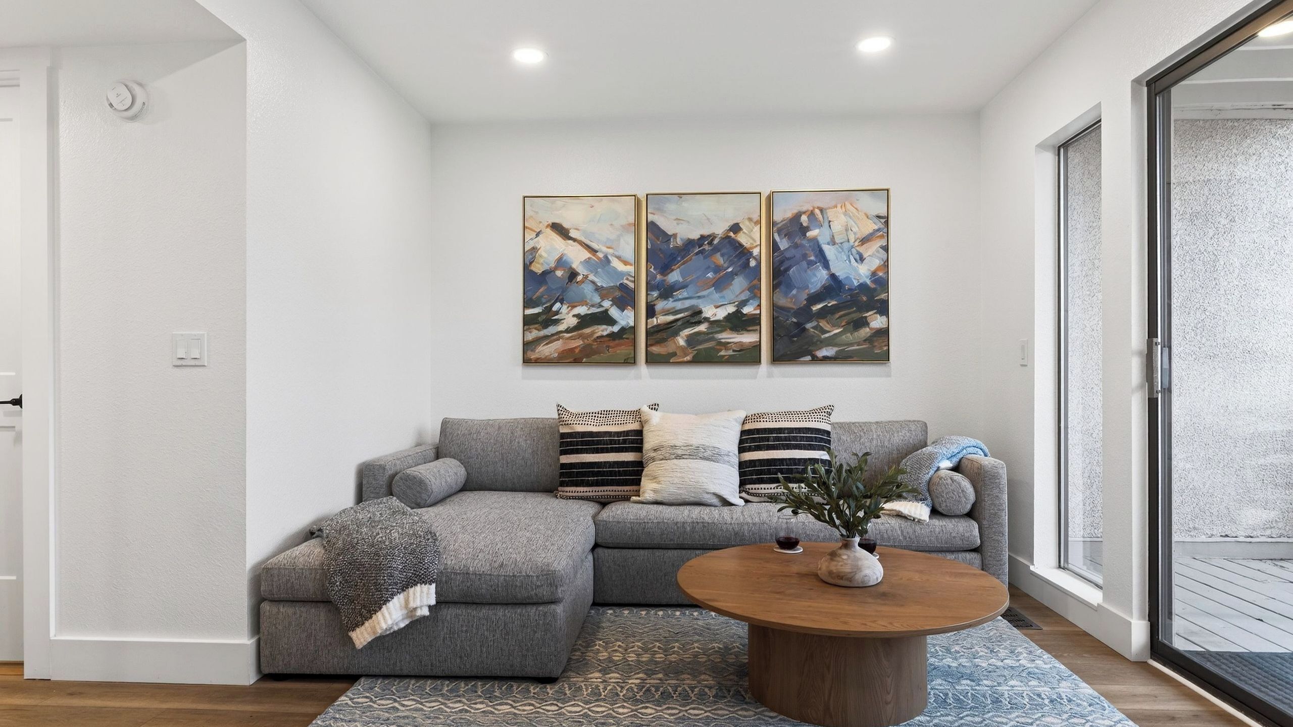 Ein modernes Wohnzimmer mit einem grauen Ecksofa, einem Holztisch und abstrakten Bildern an der Wand.