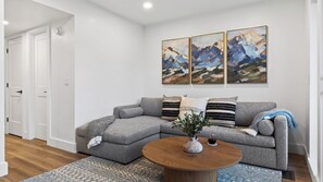 Una sala de estar moderna con un sofá seccional gris, una mesa de centro redonda de madera y una alfombra estampada.
