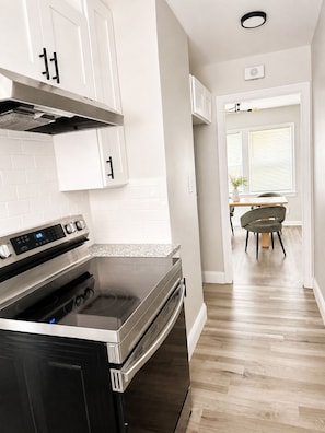 A modern kitchen with white cabinetry, a stainless steel stove, and a wooden floor.