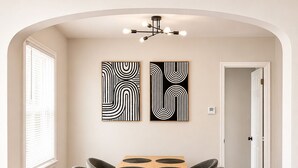 A dining area with a wooden table and four grey chairs, two abstract paintings on the wall, and a modern chandelier. - 2-bedroom apartment in enjoyable University Heights (University Heights)