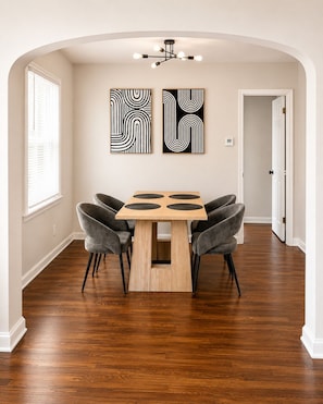 A dining area with a wooden table and four grey chairs, two abstract paintings on the wall, and a modern chandelier. - 2-bedroom apartment in enjoyable University Heights (University Heights)