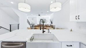 A modern kitchen with white cabinetry, a central island with a sink, pendant lighting, and a view into the dining area. - Luxury Townhome, close to the Bay, short drive to the Beach, Sleeps 10 (Santa Rosa Beach)