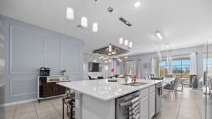 A modern kitchen with a central island, pendant lighting, and a large window offering a view. - Ultimate Disney Getaway | 12BR Bella Vida 30+ (Kissimmee)