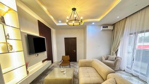 Een moderne woonkamer met een modulaire bank, een glazen salontafel, een aan de muur bevestigde televisie en een plafondlamp.