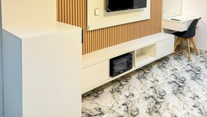 Een moderne woonkamer met een flatscreen-tv bevestigd aan een houten paneelwand, een wit bureau met een stoel en een ingebouwde magnetron.