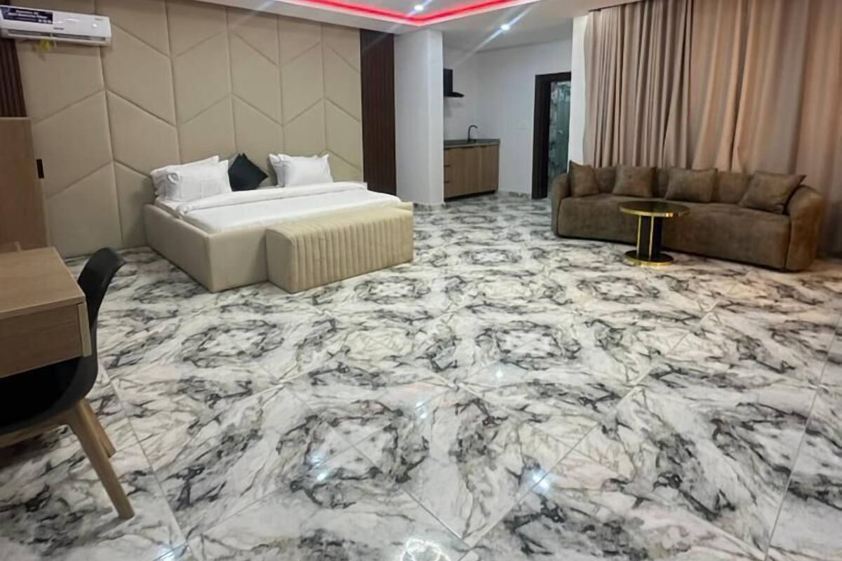 A modern hotel room with a marble floor, a bed with white linens, a sofa, a small table, and a desk.