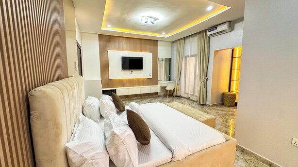 Een moderne hotelkamer met een groot bed, een flatscreen televisie aan de muur, een bureau met stoel, en een badkamer met douche en toilet.