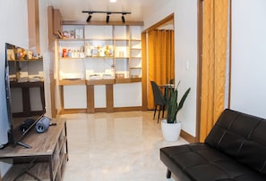 Ein Wohnzimmer mit einer Couch, einem Couchtisch, einem Fernseher, einem Bücherregal und einem Blumentopf.