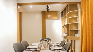 A dining area with a table set for four, chairs, a coffee pot, and a shelf with decorative items. - Cozy 2-bedroom house in amazing Legazpi City with AC, Fast Wifi & Kitchen (Legazpi City)