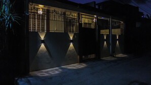 A building with a gated entrance and illuminated wall lights. - Cozy 2-bedroom house in amazing Legazpi City with AC, Fast Wifi & Kitchen (Legazpi City)
