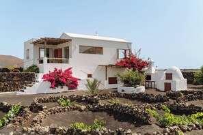 A white building with a stone wall, a wooden pergola, and pink bougainvillea. - Canaryislandshost I Camellera II (Masdache)