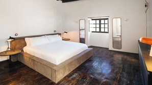 Una camera da letto con un letto grande, un soffitto in legno, un tavolino con una lampada, un comò e una finestra vista.
