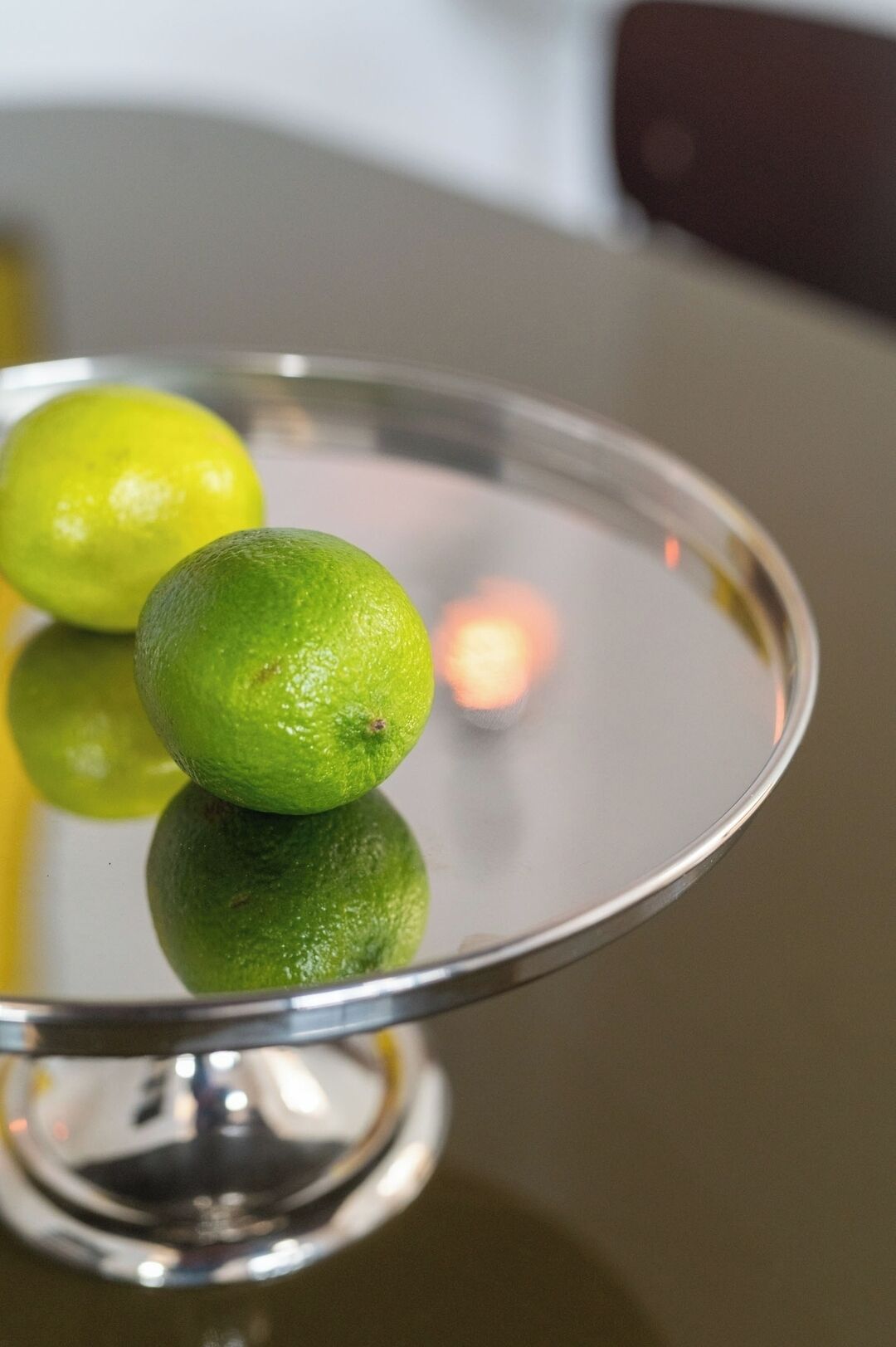 A metallic tray with two green limes on a reflective surface.