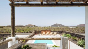 Ein Poolbereich mit Liegestühlen, einer Pergola und Blick auf eine Vulkanlandschaft.