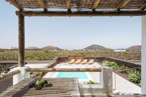 Un espace piscine avec des chaises longues, une pergola et une vue sur un paysage volcanique.