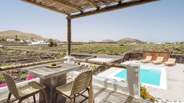Eine Terrasse mit Pool, zwei Korbstühle, einem Tisch und Blick auf eine ländliche Landschaft mit weißen Gebäuden und Bergen.