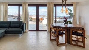 Un vaste espace de vie comprenant un canapé moderne, une table à manger en bois et de grandes fenêtres offrant une vue sur la mer et les montagnes.
