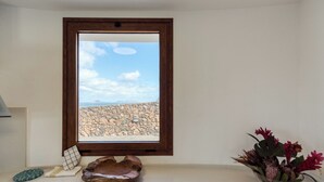 Une pièce avec vue sur un paysage rocheux, visible à travers une fenêtre, une petite table sur laquelle se trouvent un bol et un vase rempli de fleurs.