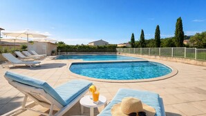 Una piscina con sillones de descanso y una tumbona, rodeada de una valla y árboles.