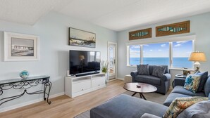 A living room with a TV, sofa, and a view of the ocean. - Oceanfront Condo in Amelia Island Plantation with Pool (Fernandina Beach)