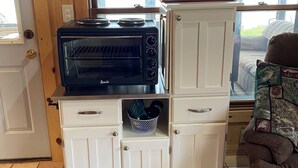A kitchenette with a built-in oven, a microwave, and a small storage cabinet with wheels.