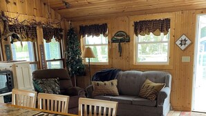 A cozy cabin interior with a dining table, a couch, and a Christmas tree.