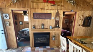 A rustic cabin interior with a checkered floor, a fireplace, a wooden ceiling with decorations, and a sign that reads 'EAT SLEEP FISH.'