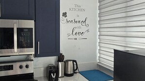 Una cocina moderna con armarios azul oscuro, un microondas de acero inoxidable, una estufa negra y un refrigerador negro. Hay un tapete azul sobre la encimera y un adhesivo en la pared que dice 