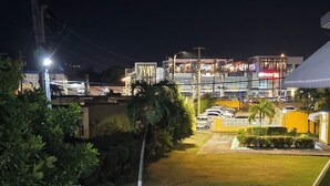 Vista nocturna de un patio de hotel con césped cuidado, un sendero y un edificio con señalización iluminada al fondo.
