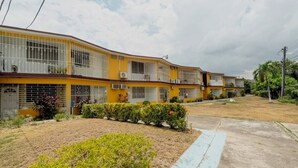 Un edificio amarillo de varios pisos con balcones, unidades de aire acondicionado y un césped bien cuidado.