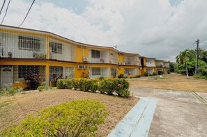 A yellow multi-story building with balconies, air conditioning units, and a well-maintained lawn. - Safe Haven Studio apartment with AC in vibrant Kingston (Kingston)