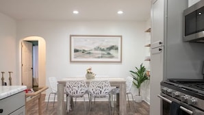 Una cocina moderna con comedor, que presenta piso de madera, armarios blancos y un cuadro grande sobre la mesa.