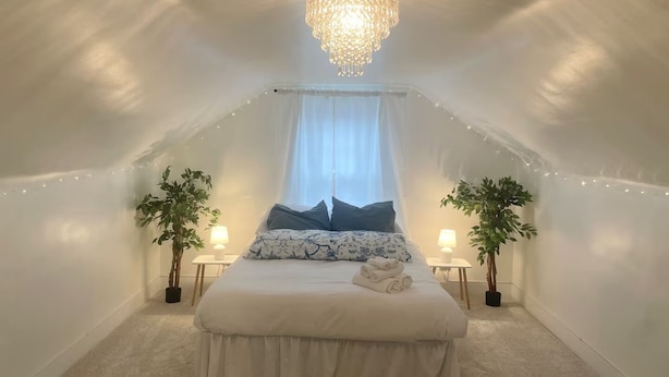 Un dormitorio con una cama grande, dos mesitas de noche con lámparas, una araña y luces de cadena.