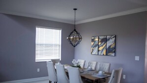 Une salle à manger avec une table dressée pour six personnes, un lustre et une fenêtre avec des stores.