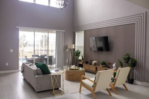 Ein geräumiges Wohnzimmer mit einer Couch, Sesseln, einem Fernseher und einem großen Fenster.