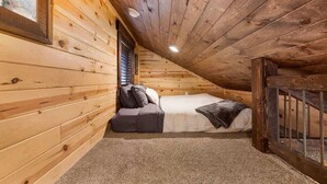 Een knus zolderkamer met een houten schuine plafond, een enkel bed en een zithoek met kussens.