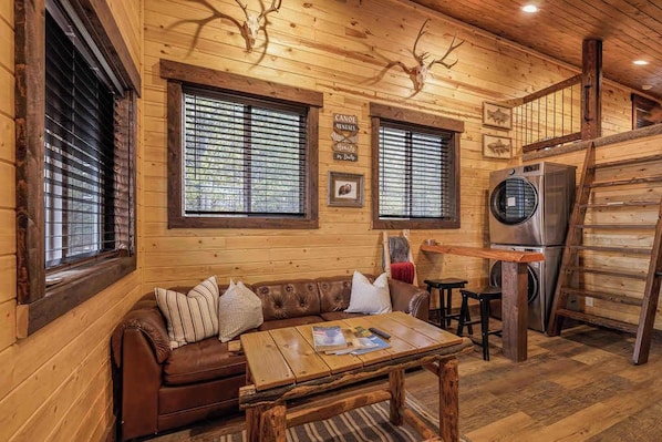 A wooden cabin interior with a brown leather sofa, a wooden table, and a refrigerator.