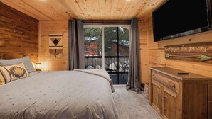 Een gezellig houten slaapkamer met een groot bed, een televisie en uitzicht op een besneeuwd landschap door een schuifdeur.