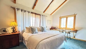 Une chambre à coucher comprenant un lit, une table de chevet, une lampe, un ventilateur et un bureau avec une chaise.
