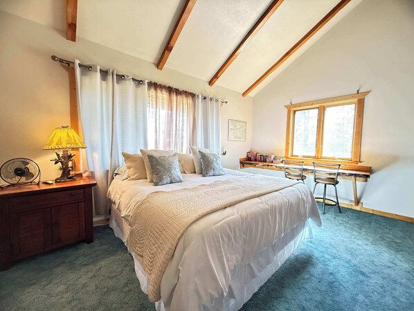 Un dormitorio con cama, mesita de noche, lámpara, ventilador y escritorio con silla.