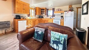 Un salon chaleureux avec un canapé en cuir, des meubles en bois et une cuisine en arrière-plan.